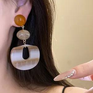 Detailed shot of large acrylic marble drop earrings with amber stud worn on ear
