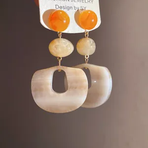 Close-up of acrylic drop earrings with orange beads and marble texture pendants