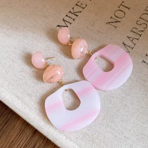 Close-up of marbled pink acrylic earrings with silver needle studs on canvas background