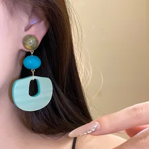 Close-up view of a three-tier acrylic drop earring with marble finish and mint green pendant