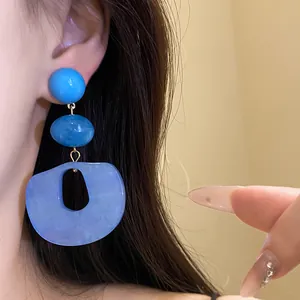 Close-up view of blue acrylic drop earrings featuring abstract geometric shapes on model's ear.