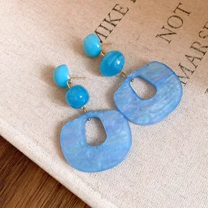 Macro view of blue acrylic geometric dangle earrings with fine marble texture detail.