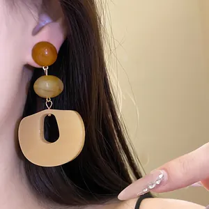 Close-up detail of acrylic drop earrings with amber and beige resin beads on model ear