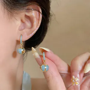 Detail of 18k gold-plated huggie earrings with a chic blue zircon sphere drop.