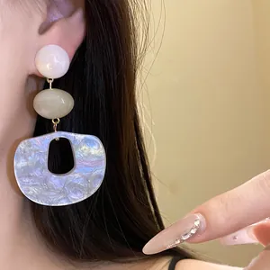 Detailed macro view of iridescent acrylic triple-drop earrings worn by a model's ear.