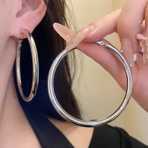 Detailed view of large polished silver-tone circular hoop earrings on model and hand