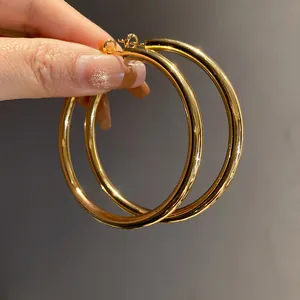 Detailed macro shot of elegant large gold metallic hoop earrings held by a hand