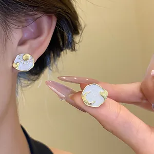 Detailed close-up of asymmetric sun and moon enamel heart stud earrings worn on ear.