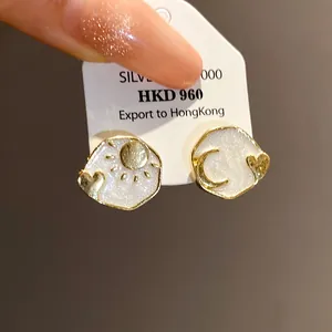 Macro detail of retro sun and moon gold stud earrings with sparkling white enamel
