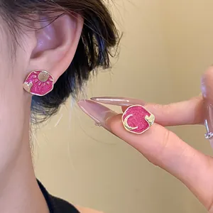 Detailed close-up of pink enamel sun and moon stud earrings held in hand.