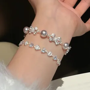 Detailopname van een elegante armband met zirkonia strikjes, parels en hartjesketting om pols