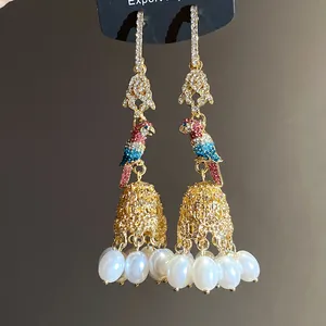 Close-up detail of luxurious gold-plated parrot earrings with vibrant rhinestones and pearls