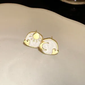 Close-up of asymmetrical sun and moon stud earrings with white enamel finish