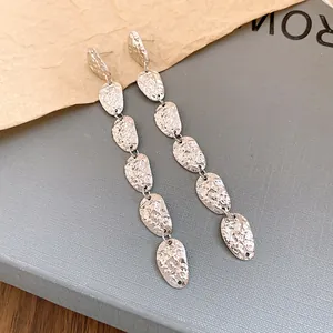 Primer plano detallado de pendientes largos de metal plateado con diseño de arrugas