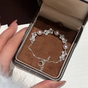 Detailopname van een verstelbare armband met zirkonia strikjes en parels in een geschenkdoos.