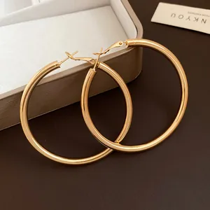 Close-up of large gold round metal hoop earrings on a light gray jewelry box.