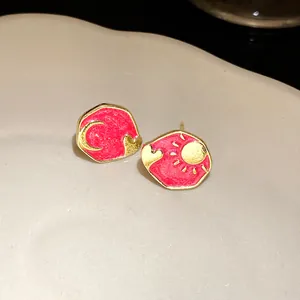 Detailed close-up of gold-plated enamel sun and moon stud earrings with heart detail