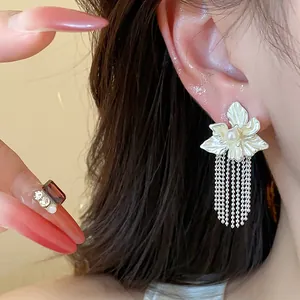 Close-up detail of floral stud earrings with pearls and long chain tassels.