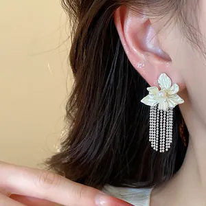 Detailed close-up of elegant flower stud earrings with long pearl and metal tassels