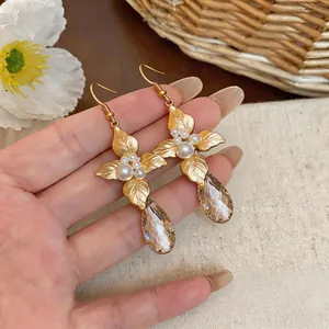 Close-up view of vintage gold-tone leaf earrings featuring white pearls and teardrop crystals