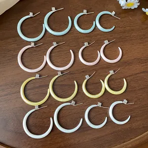 Detalle de pendientes esmaltados en forma de C con circonita sobre madera oscura.