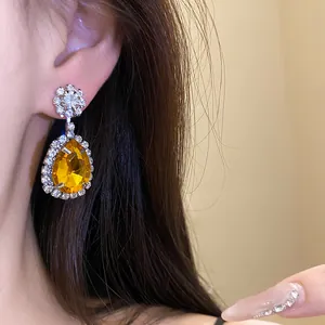 Detailed close-up showing an elegant yellow teardrop gemstone earring worn by a model