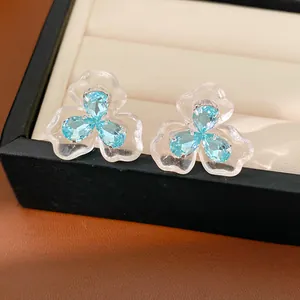 Close-up of elegant flower stud earrings with blue zircons and clear resin petals