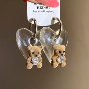 Detailed macro shot of flocked teddy bear earrings featuring clear heart pendants.