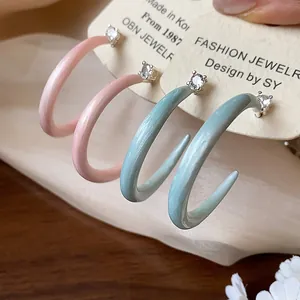 Primer plano de pendientes de aro en C de esmalte rosa y verde menta con circonita.
