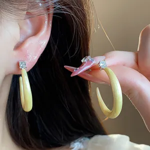 Detalle macro de elegantes pendientes de esmalte crema en forma de C con circón