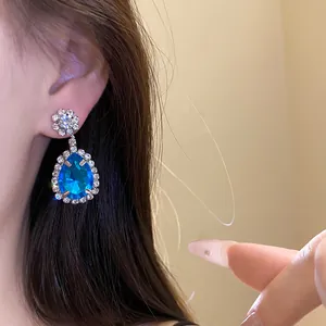 Close-up of elegant blue teardrop pendant earrings with rhinestones worn by a model.
