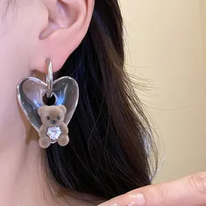 Detailed shot of a cute flocked bear earring with a clear acrylic heart pendant.