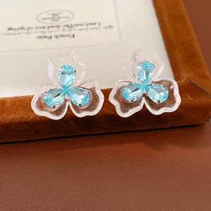 Close-up of light blue zircon and clear resin flower stud earrings on brown velvet