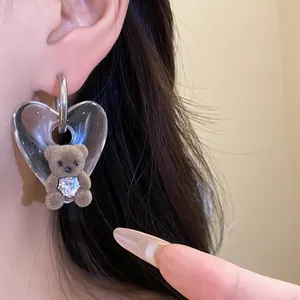 Close-up of cute flocked bear earrings with heart rhinestone on transparent pendant.