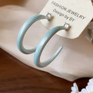 Detalle de pendientes de botón en forma de C de esmalte azul claro con circonitas