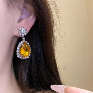Detailed macro shot of luxury yellow teardrop earring with halo diamond setting on model.