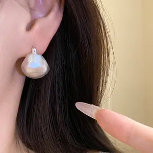 Close-up detail of brushed silver semi-circular earrings worn on a model's ear lobe