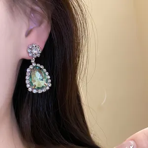 Close-up of elegant green teardrop rhinestone earrings worn on ear showing fine details.