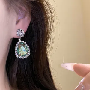 Close-up detail of green teardrop dangle earrings with sparkling rhinestone halo
