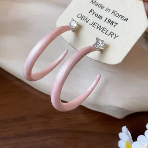Detalle macro de pendientes de botón en forma de C de esmalte rosa con circón en tarjeta