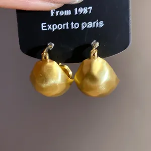 Detailed close-up view of brushed gold semi-circular earrings on a black display card