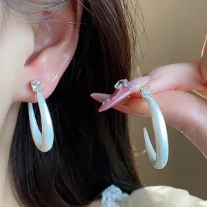Detalle de los pendientes de aro en C de esmalte blanco con aguja de plata y circón