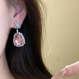 Close-up of elegant pink teardrop dangle earrings with crystal halo on model.