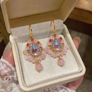 Gros plan de boucles d'oreilles élégantes en zircon rose avec pompons dans un écrin crème