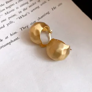 Close-up of elegant gold brushed half-round hoop earrings on a vintage book page.