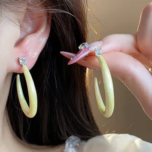 Detalle de pendientes de aro en C de esmalte verde claro con circonitas brillantes