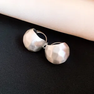 Close-up detail of brushed silver semi-circular earrings showing fine metallic texture.