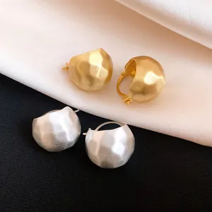 Macro detail of gold and silver brushed metal semi-circular earrings on silk fabric.