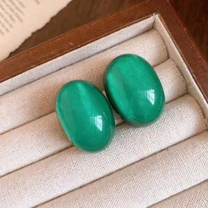 Elegant green oval resin stud earrings with silver needles in a wooden jewelry box