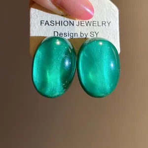 Close-up detail of green oval resin stud earrings with shimmering cat-eye effect texture